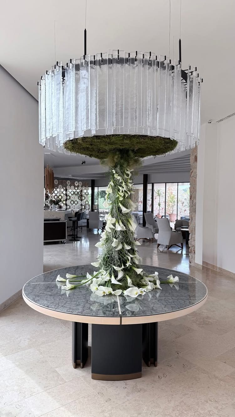 White calla lily floral sculpture rising from a marble table to a chandelier.