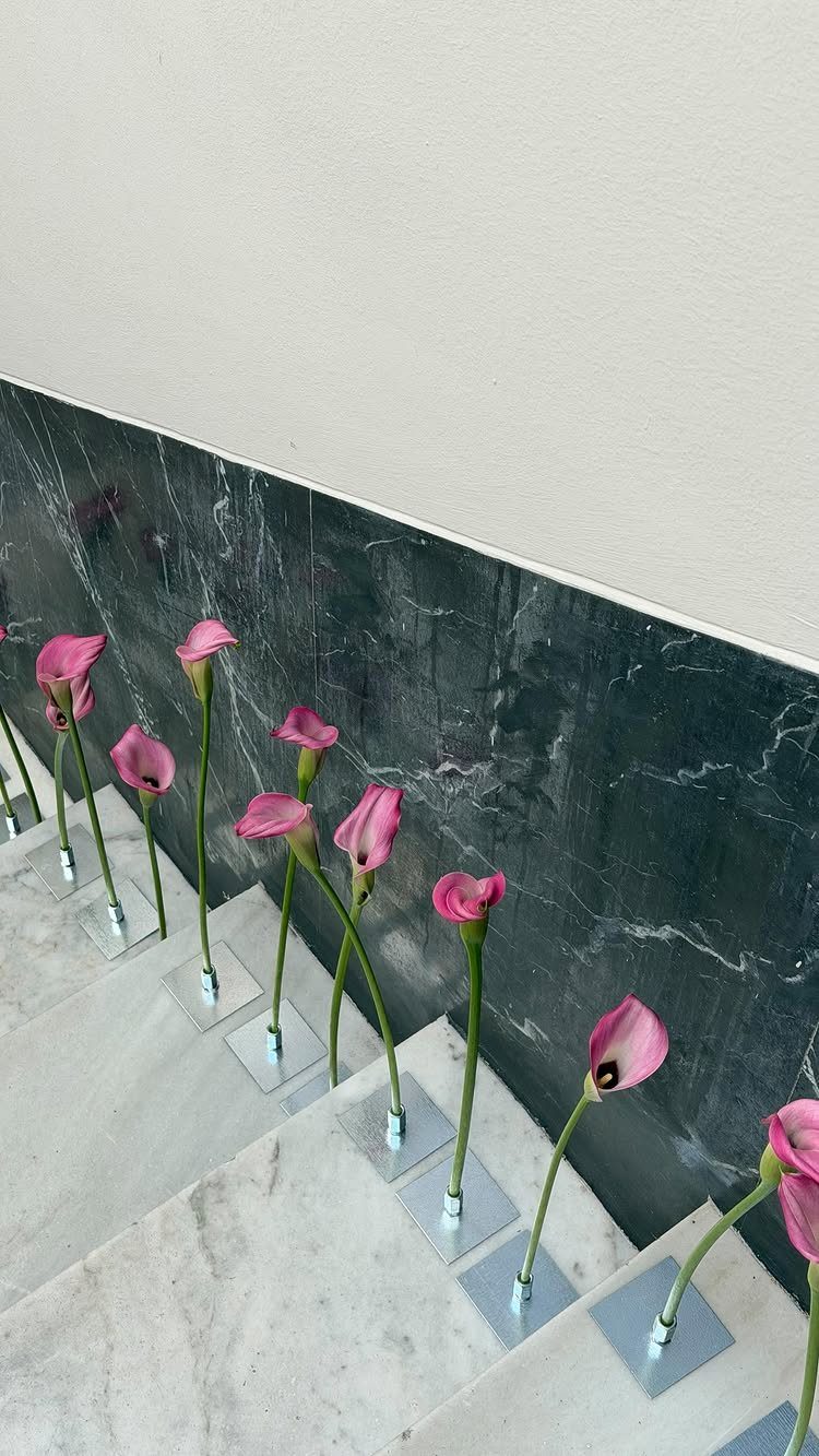 Pink calla lilies in small vases arranged along white marble stairs.
