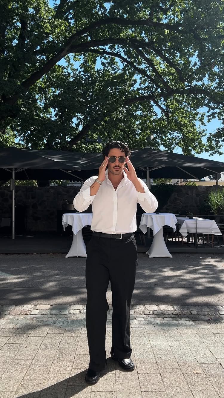 Man in white shirt and black trousers posing outdoors at a wedding venue