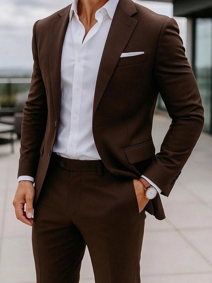 Man in a brown tailored suit and white open-collar shirt standing outdoors.