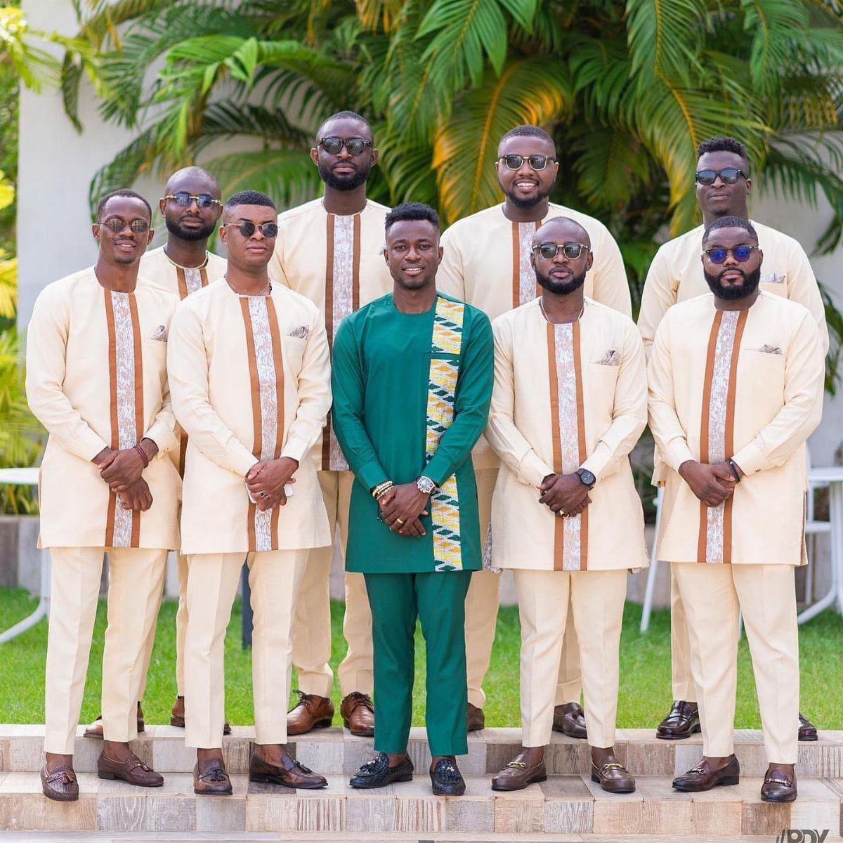 Group of men in traditional African tunics and trousers posing outdoors in sunlight.