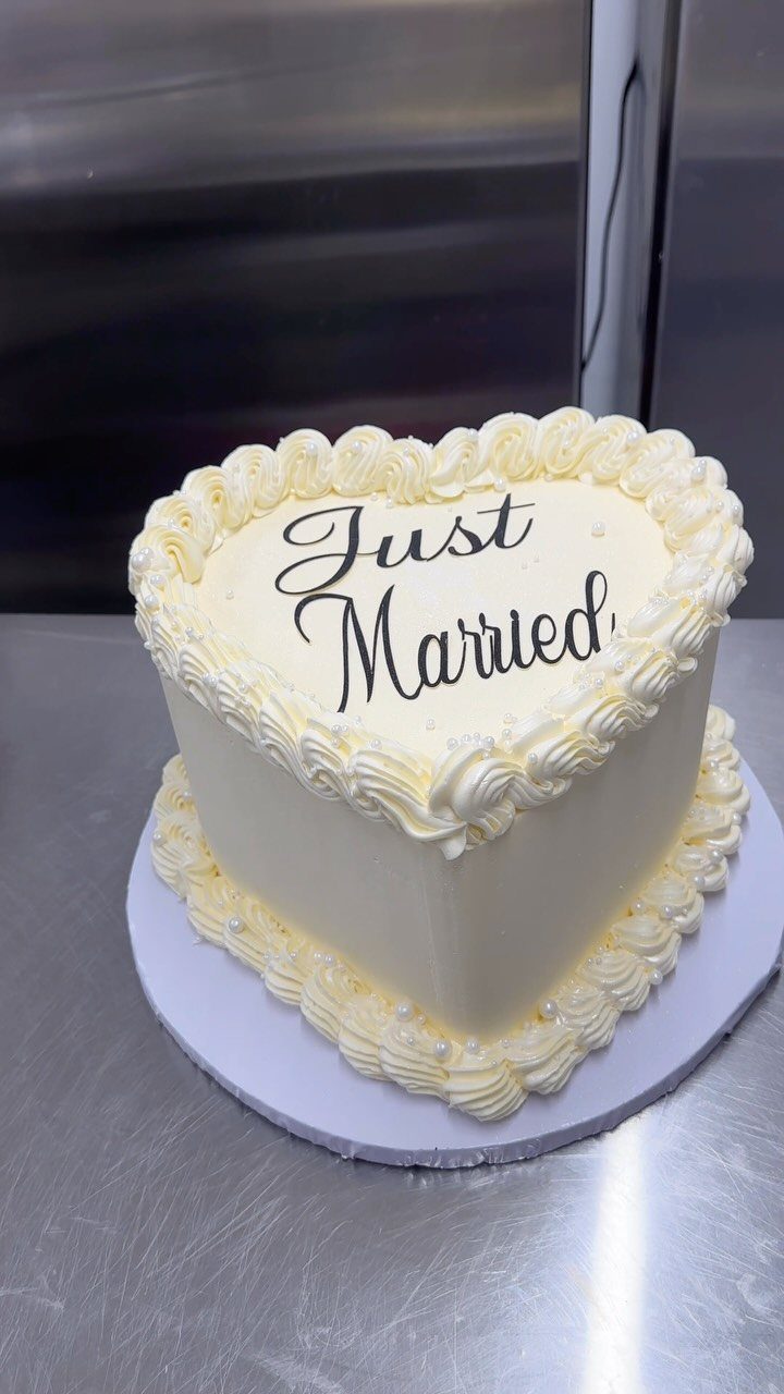 Heart-shaped white wedding cake with Just Married written in black cursive icing.