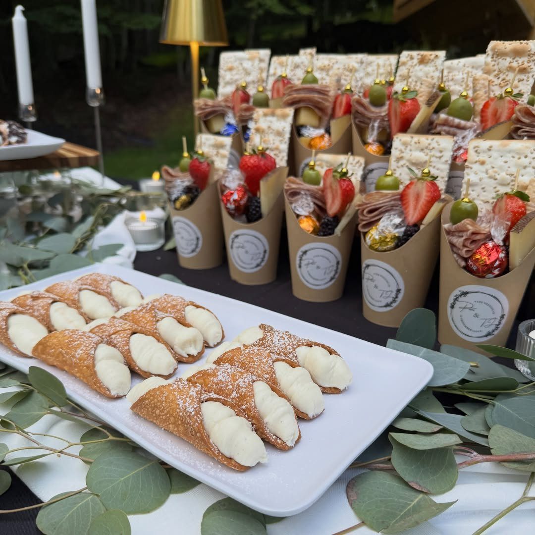 Cream-filled cannoli and charcuterie cones arranged on a table with eucalyptus leaves.