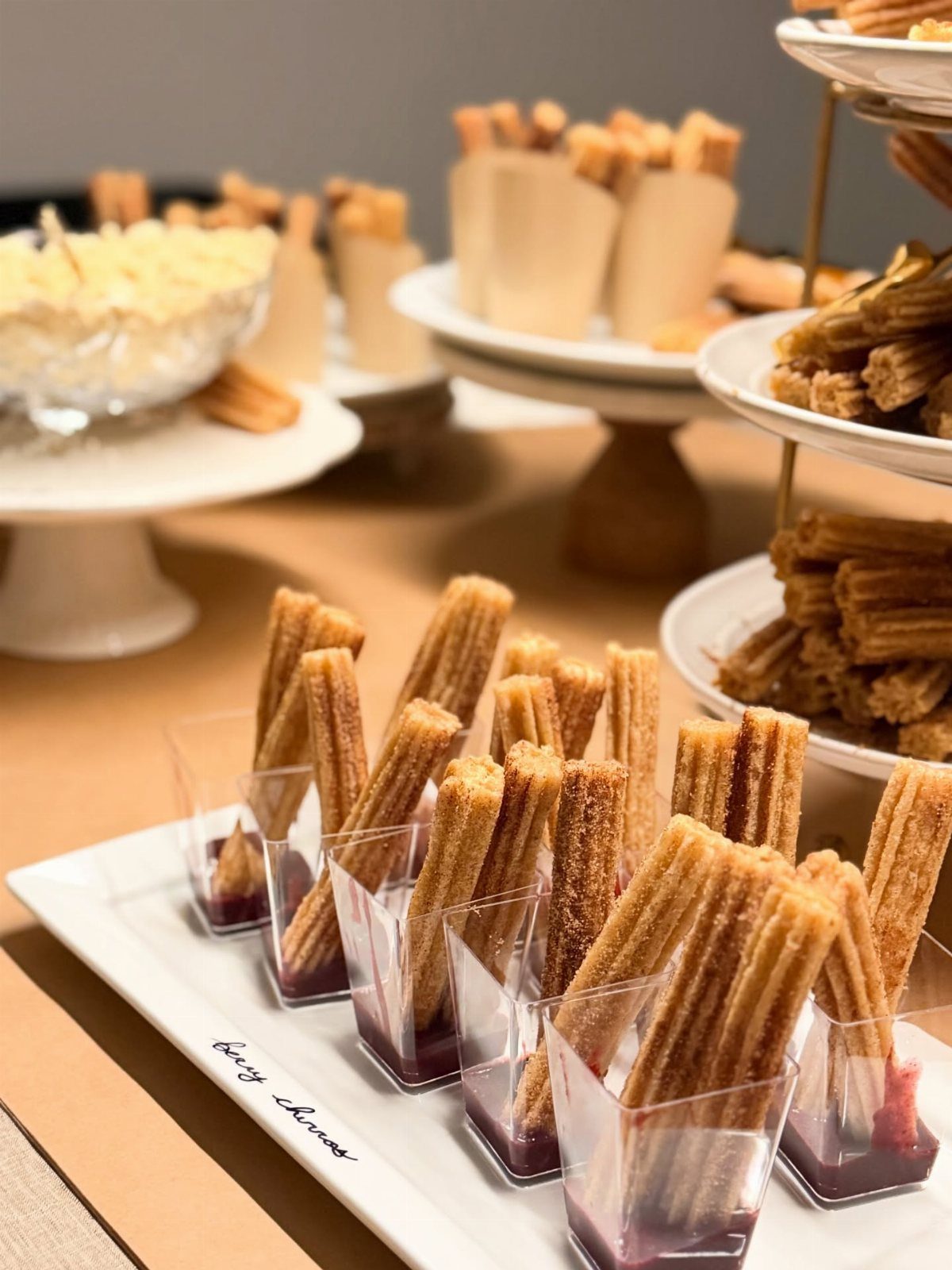 Churros in small plastic cups with red dipping sauce on a white platter.