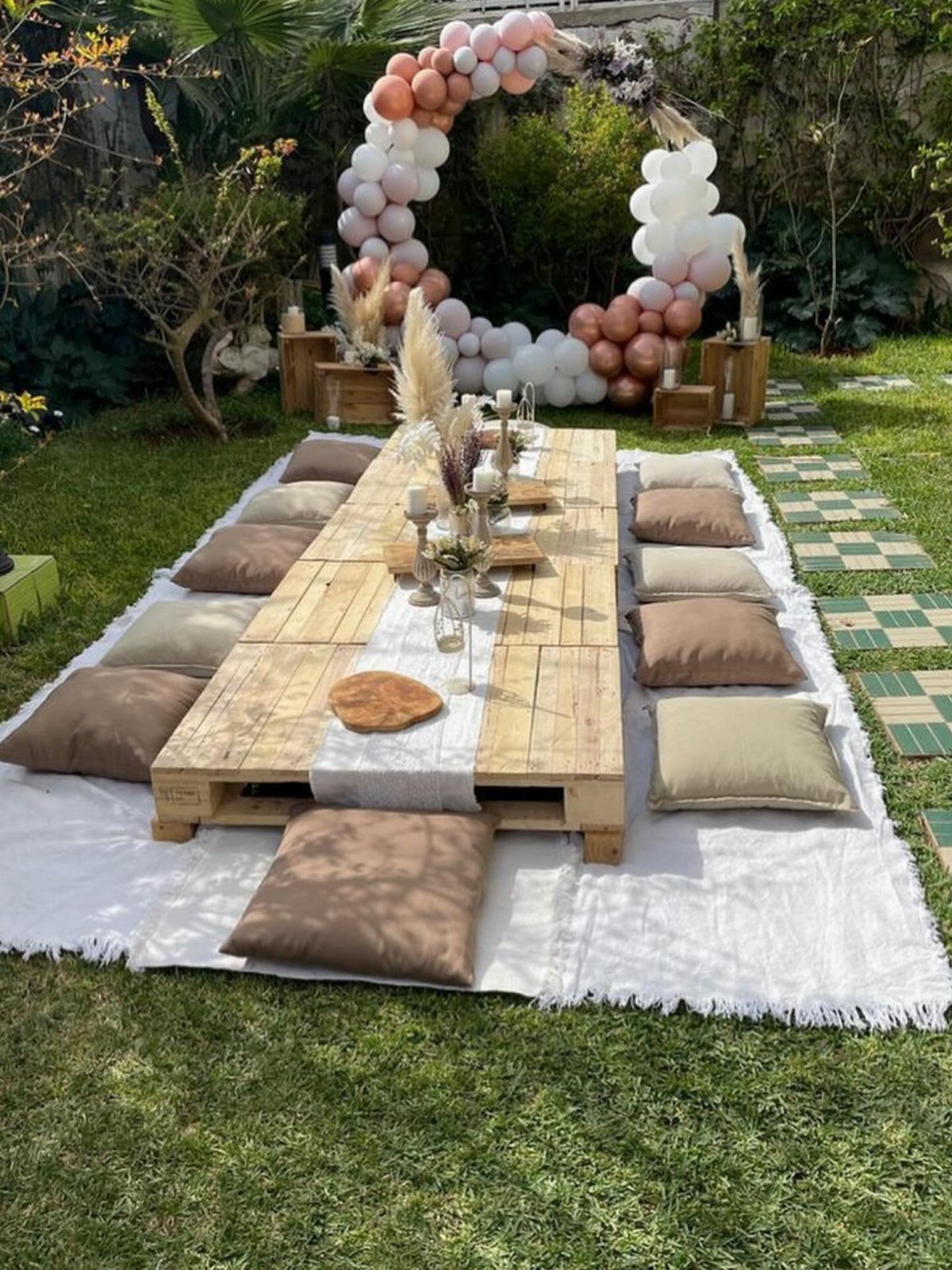 Low wooden pallet table with cushions and a balloon arch in a garden