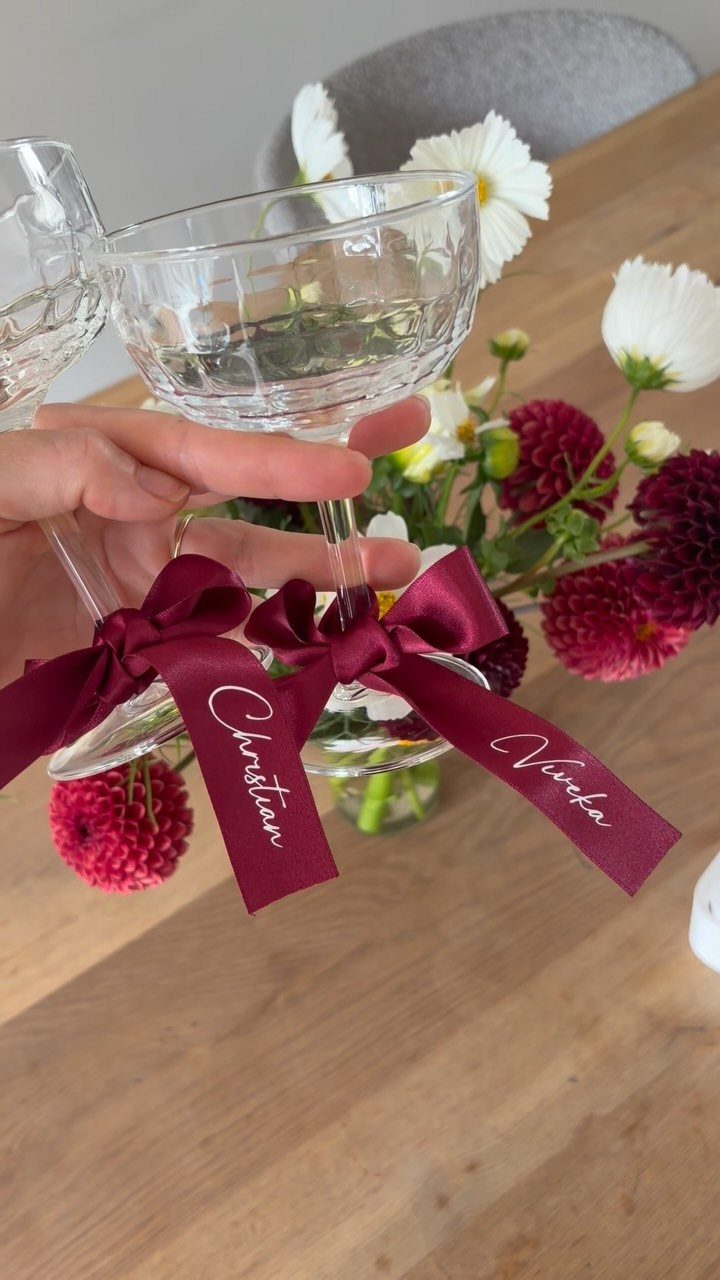 Glass coupe with burgundy ribbons featuring names Christian and Viveka on wooden table