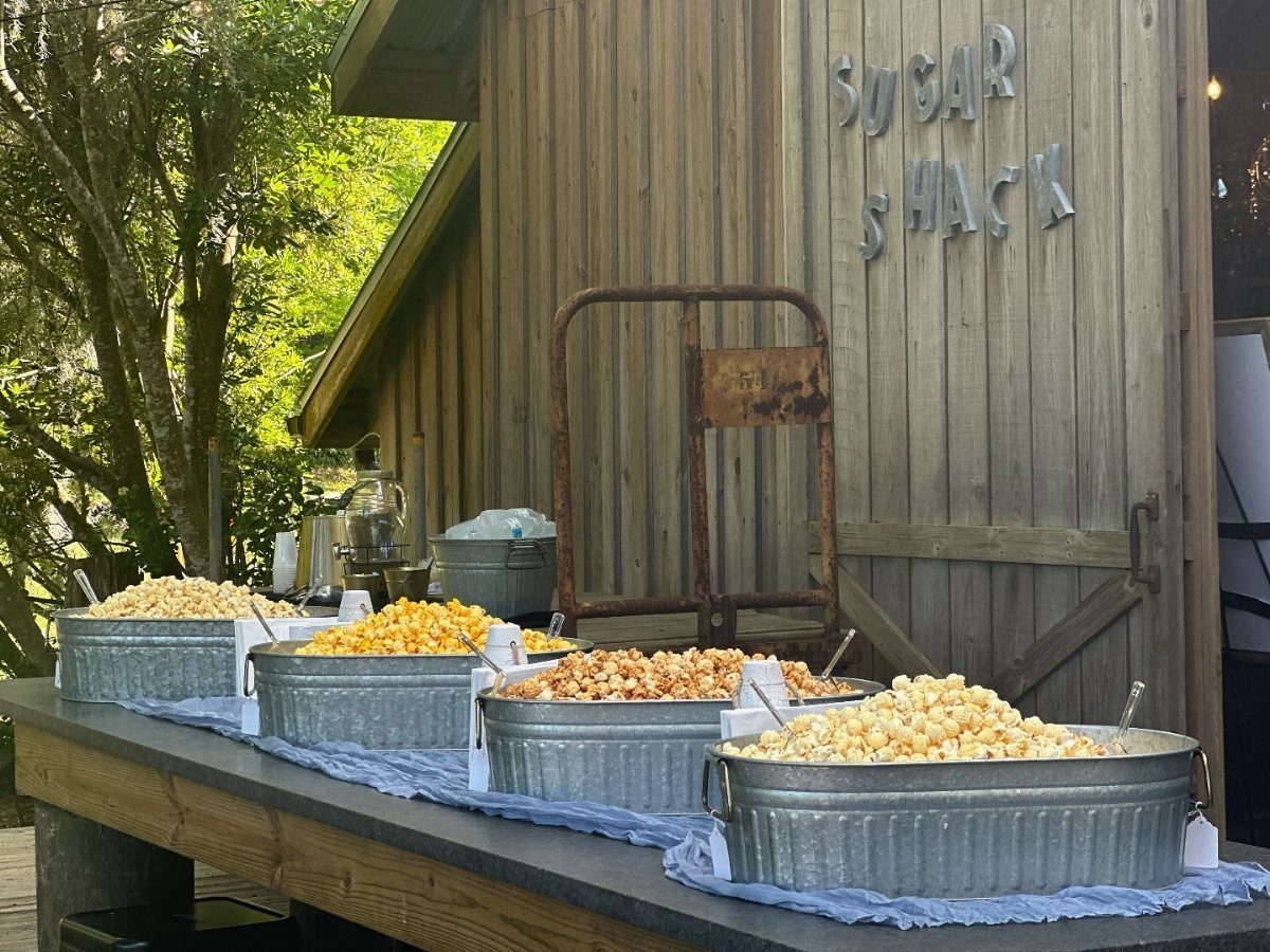 Popcorn snacks in metal tubs on a table outside a rustic wooden shack.
