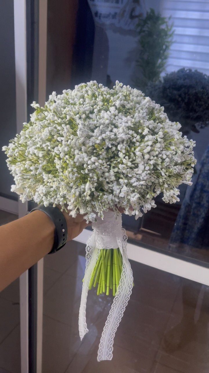 White baby's breath bridal bouquet with lace ribbon held by a hand.