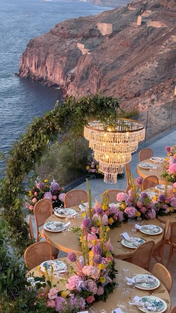Wedding reception tables with floral centerpieces on a cliff overlooking the ocean coast.
