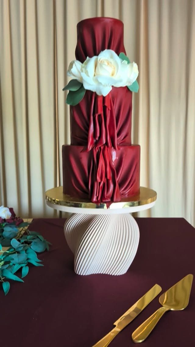 Deep red draped wedding cake with a white flower on a sculptural stand