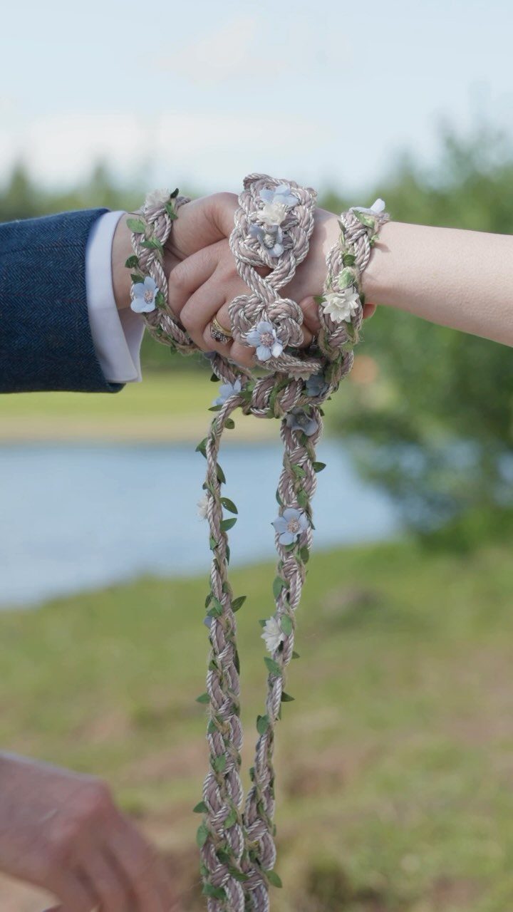 Hands of a couple bound together with a floral braided rope outdoors