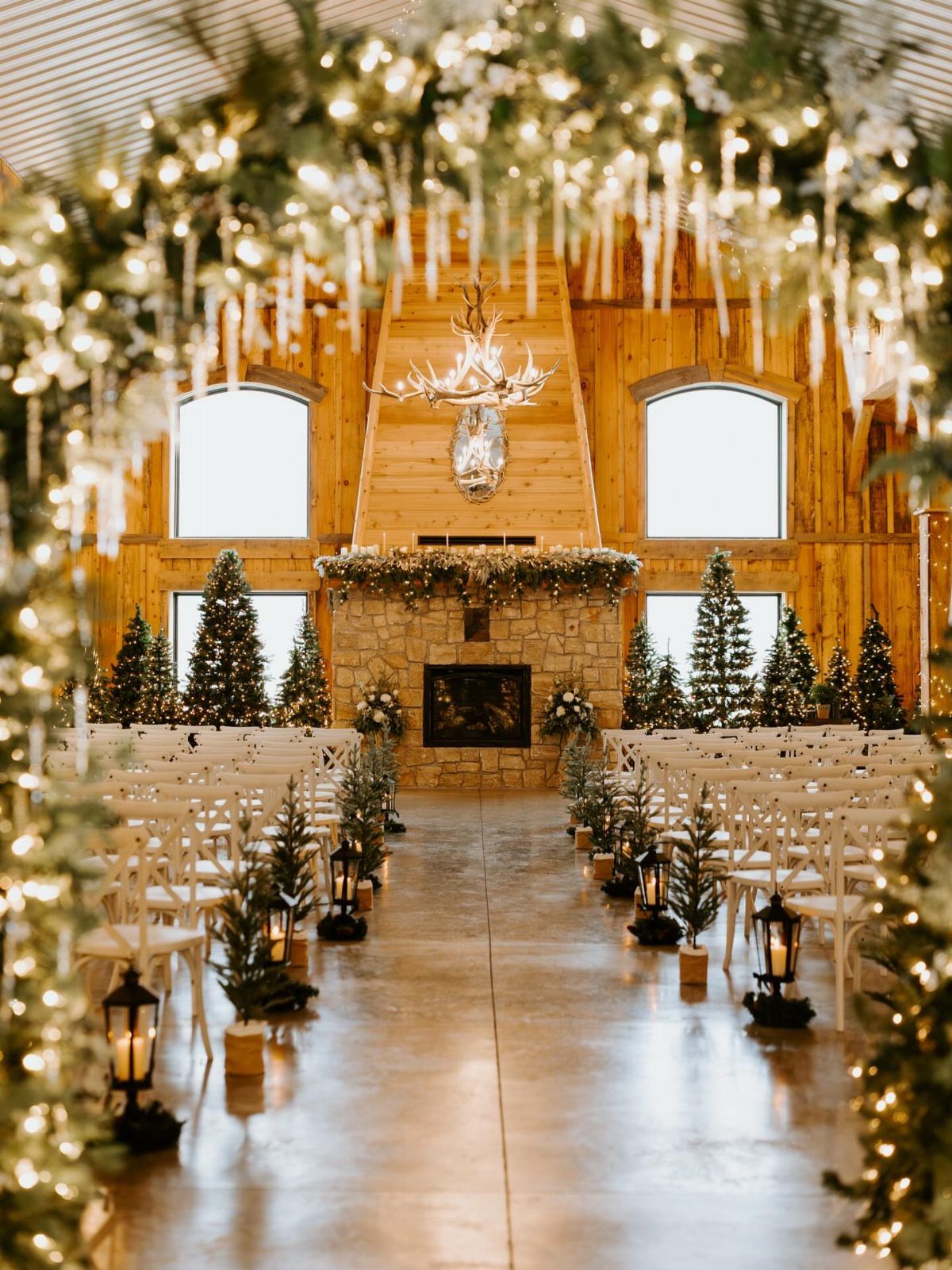 Rustic barn wedding ceremony setup with Christmas trees, lanterns, and warm string lights.
