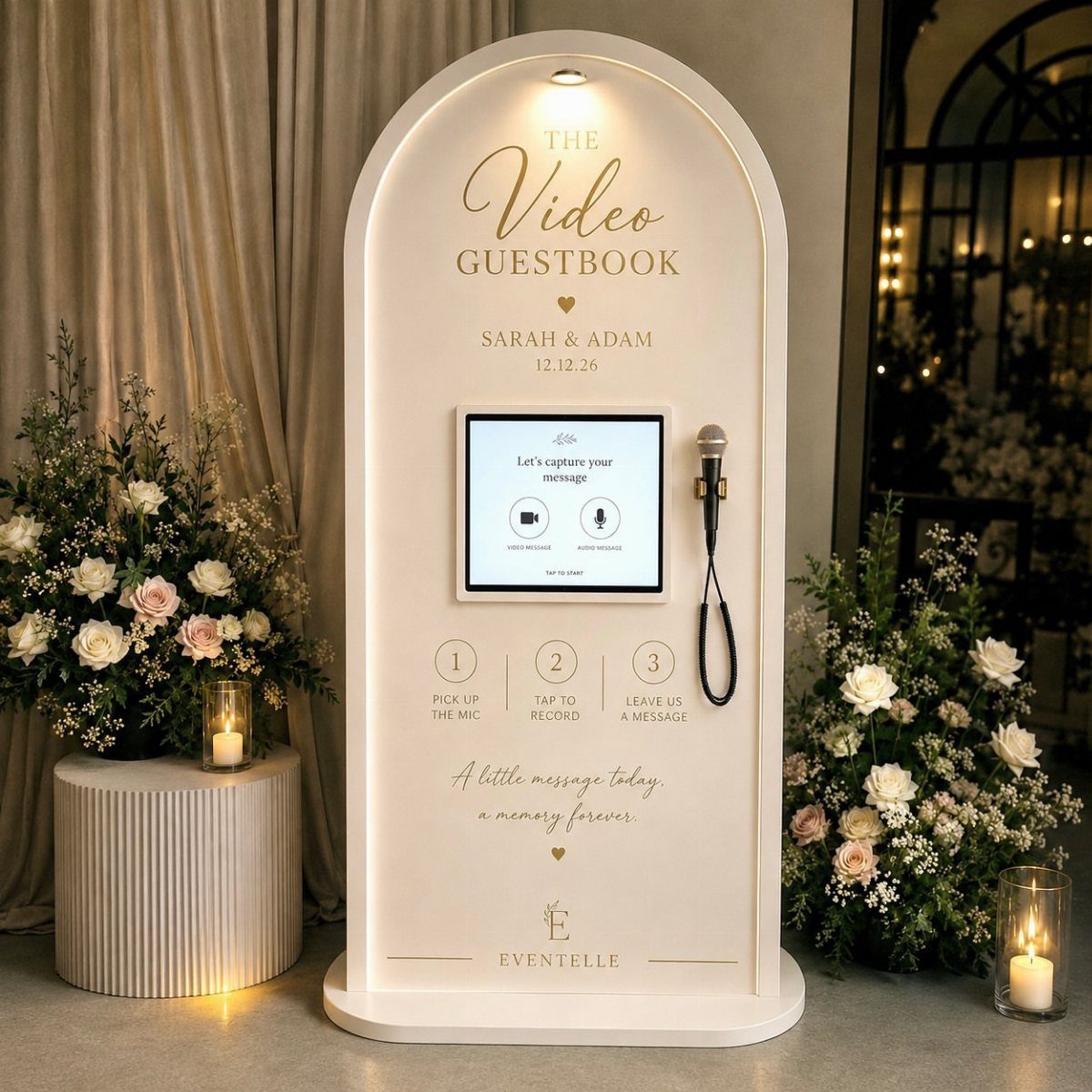 White arched video guestbook kiosk with microphone and flowers at a wedding event