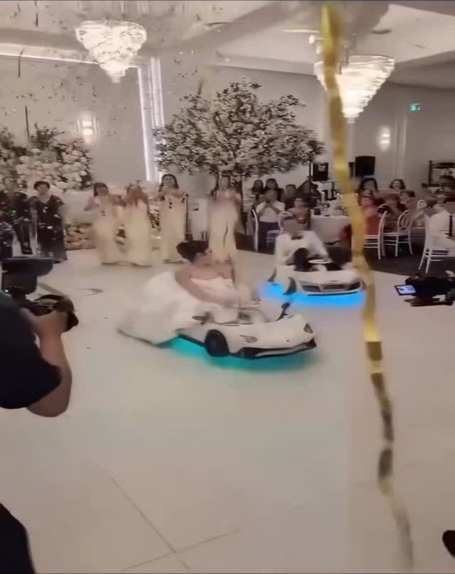 Bride and groom driving small white toy cars across a wedding dance floor