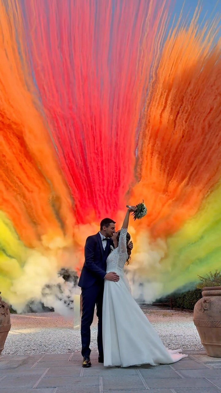 Bride and groom embracing in front of dramatic red and orange smoke bombs.
