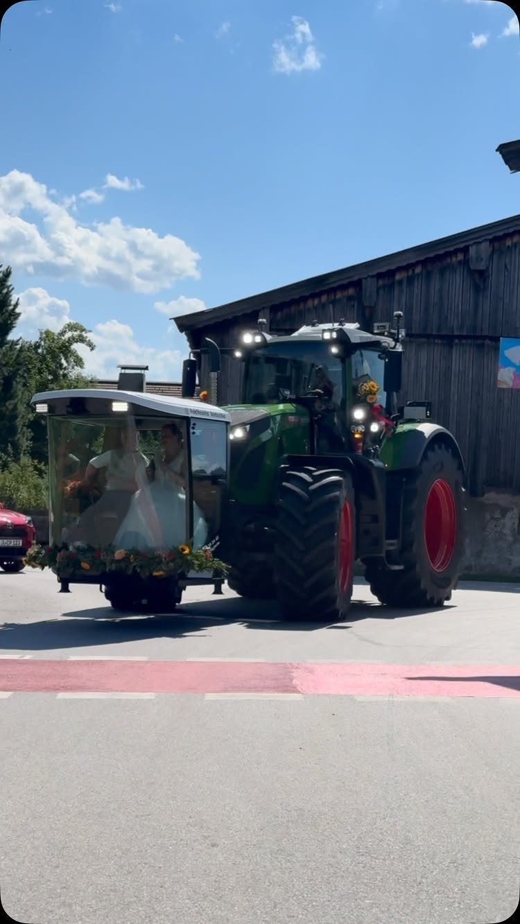 Bride in white dress riding in a flower-decorated carriage pulled by a tractor.