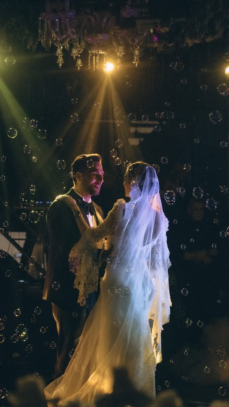 Bride and groom dancing closely under a spotlight surrounded by floating bubbles
