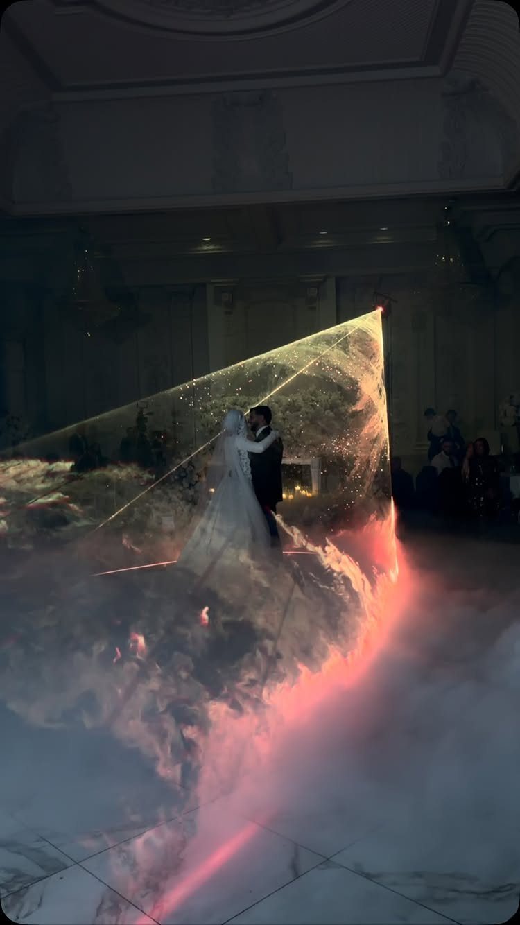 Bride and groom dancing in a fog-filled ballroom under a triangular light beam.