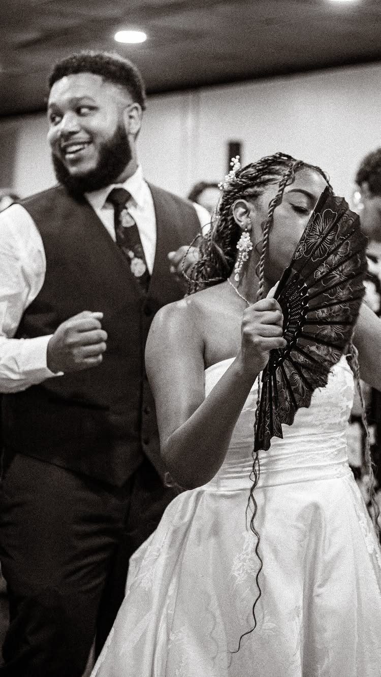 Bride with a black lace fan and groom dancing at a wedding reception.