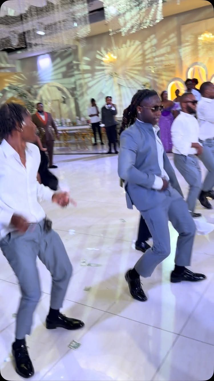 Men in grey suits dancing energetically on a white wedding dance floor.