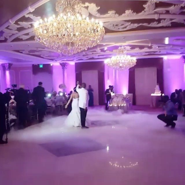 Bride and groom dancing in a ballroom with low-lying fog and chandeliers.