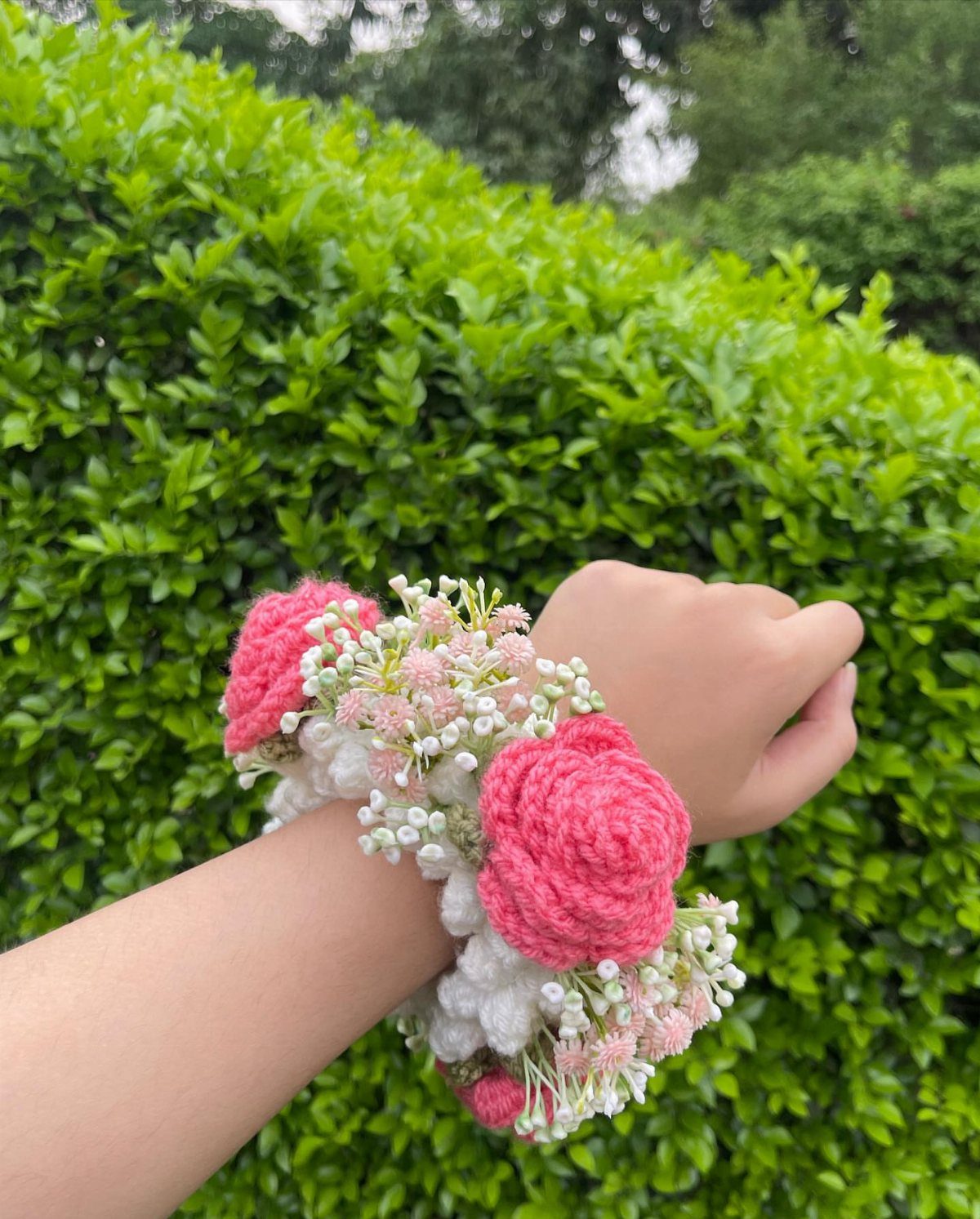 Crochet floral corsage with pink roses and white flowers on a person's wrist.