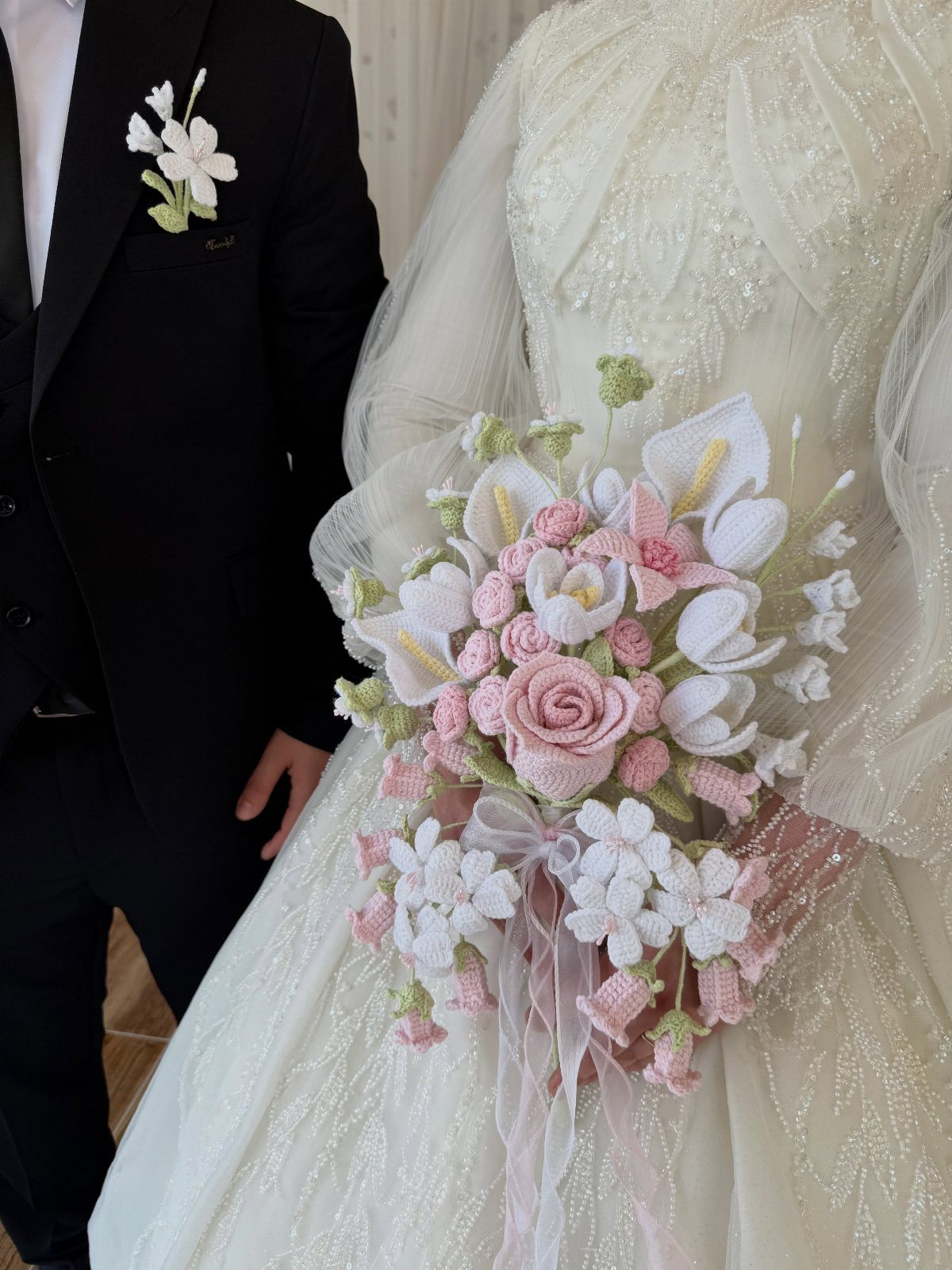 Crochet wedding bouquet of pink and white flowers held by a bride.
