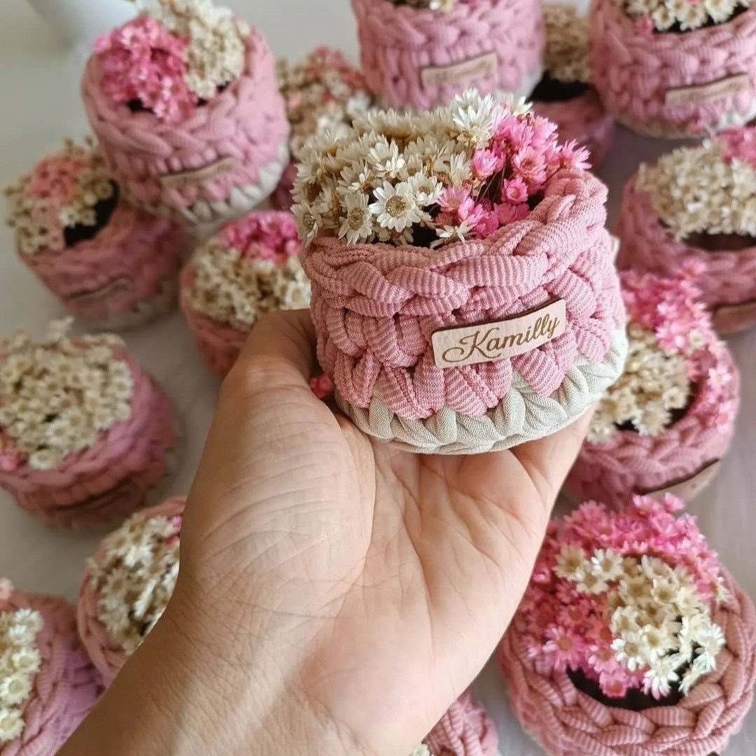 Hand holding a small pink crochet pot filled with tiny dried flowers