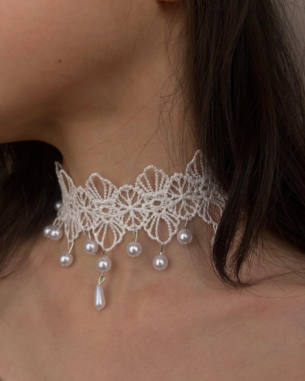 White crochet lace choker with hanging pearl beads worn around a person's neck