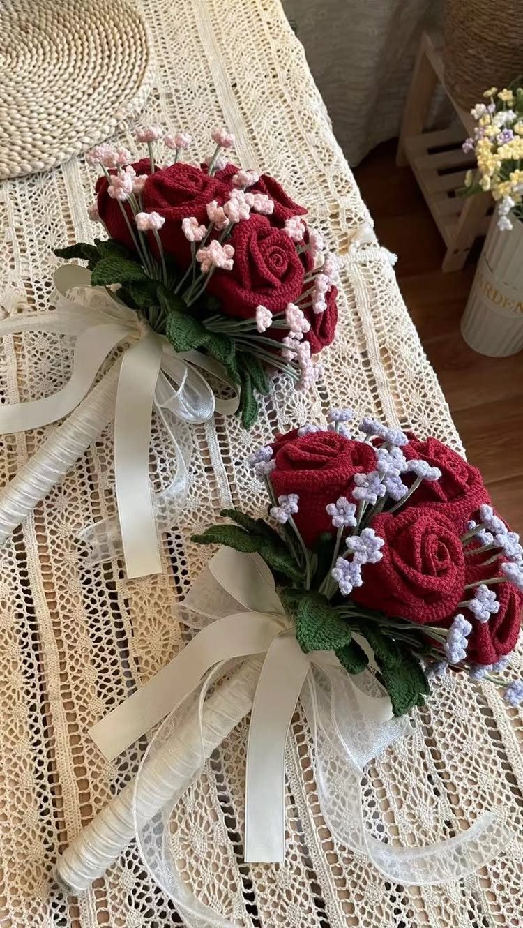 Two crochet bouquets with red roses and white ribbons on a lace tablecloth