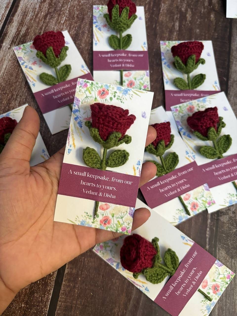 Crochet red roses attached to white wedding keepsake cards on a wooden table