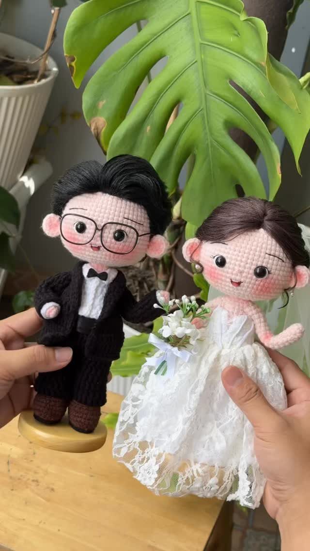 Crochet amigurumi bride and groom dolls in wedding attire held by hands.