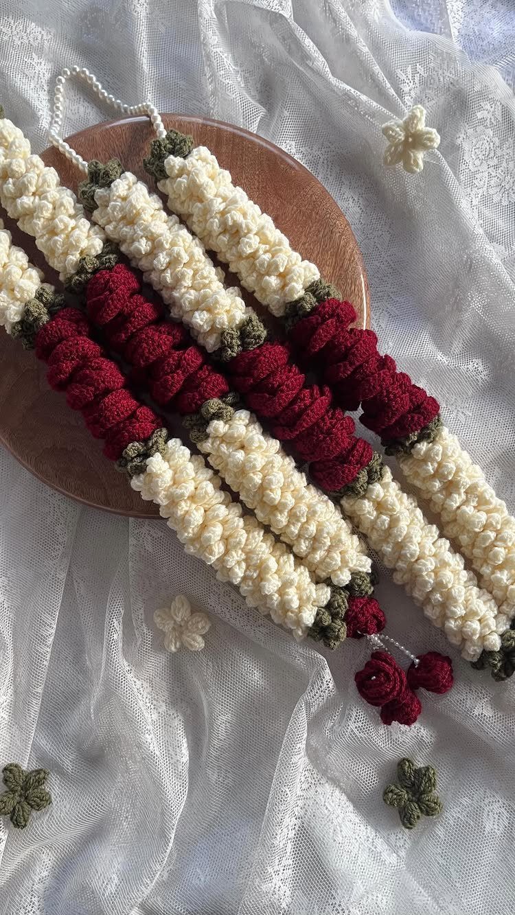 Crochet garlands in cream and red resting on a wooden plate and white fabric.