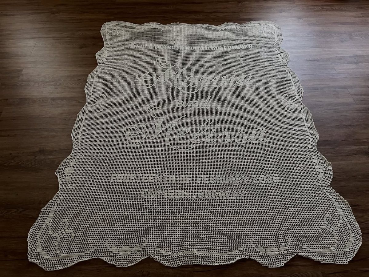 White lacy crochet wedding throw blanket with personalized names on wooden floor