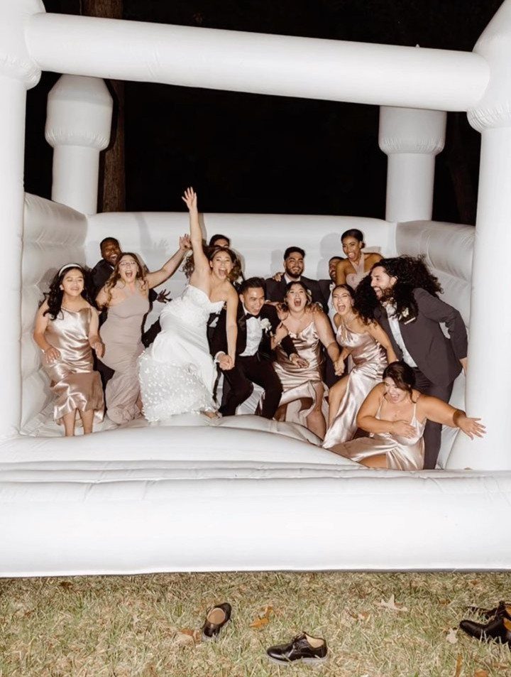 Wedding guests and bride laughing and jumping inside a white inflatable bouncy house.