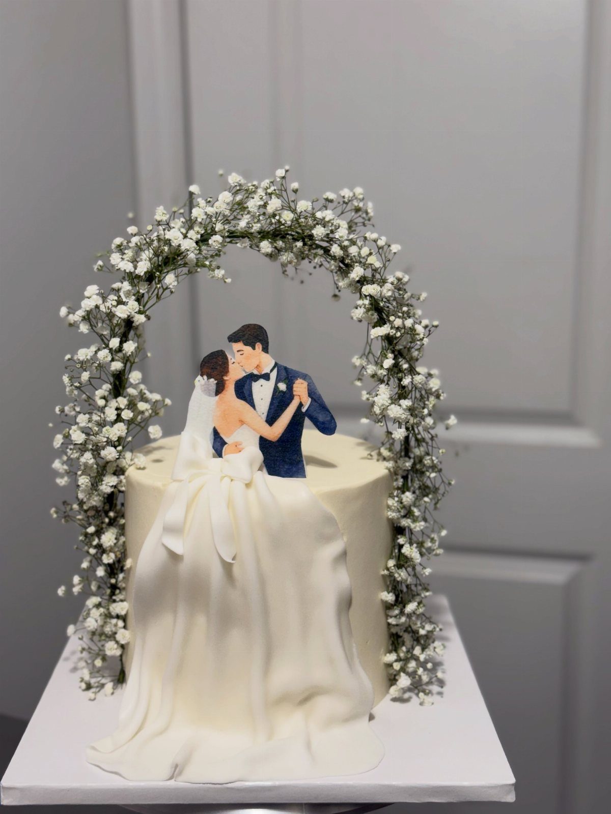 Wedding cake topper featuring a dancing couple framed by a baby's breath arch.