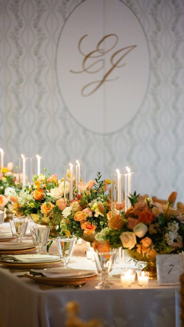 Long wedding table with orange floral centerpieces, lit candles, and a CJ monogram.