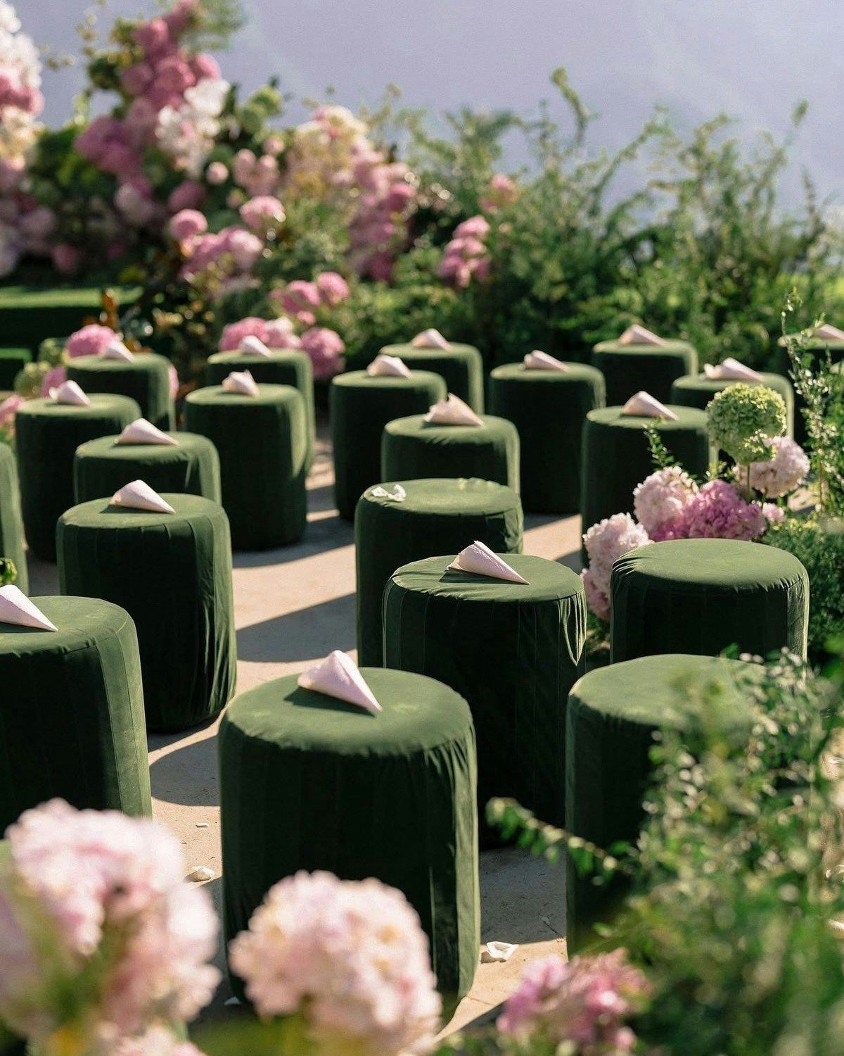 Dark green velvet floor cushions arranged as guest seating for an outdoor wedding ceremony.