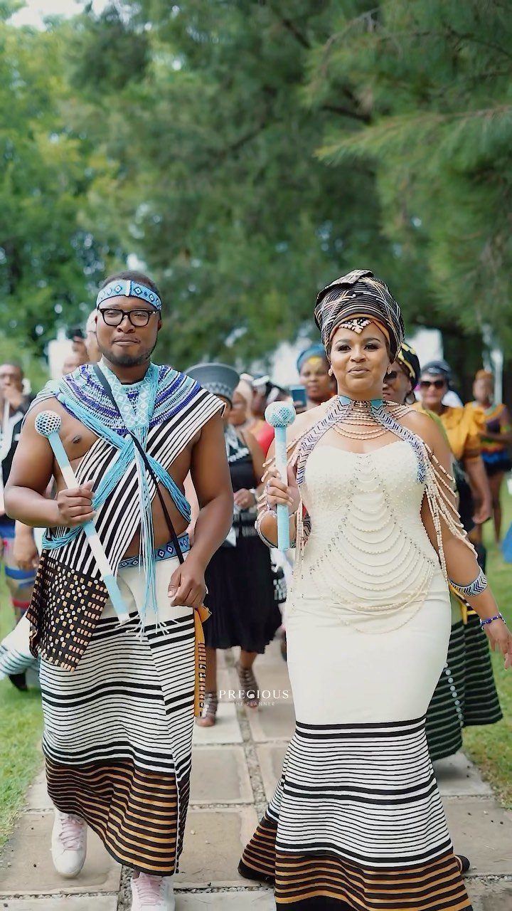 Couple in traditional African wedding attire walking outdoors on a stone path.