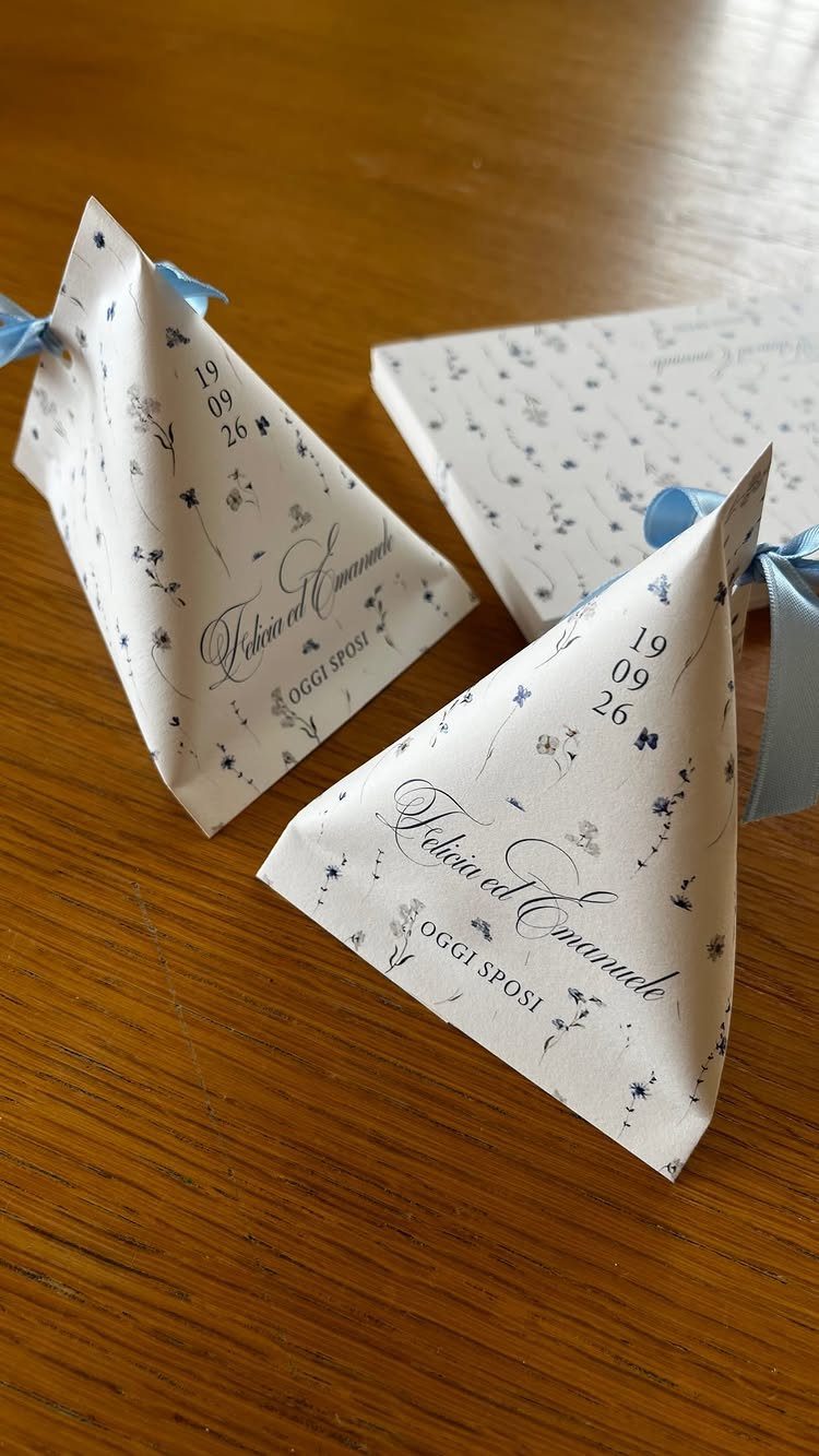 White conical wedding favor bags with blue floral prints and ribbons on wood.