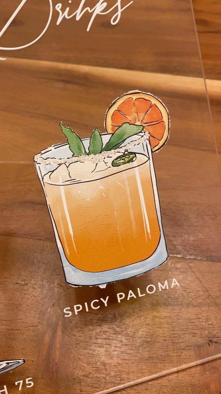 Spicy Paloma cocktail illustration on a clear acrylic sign over a wooden table.
