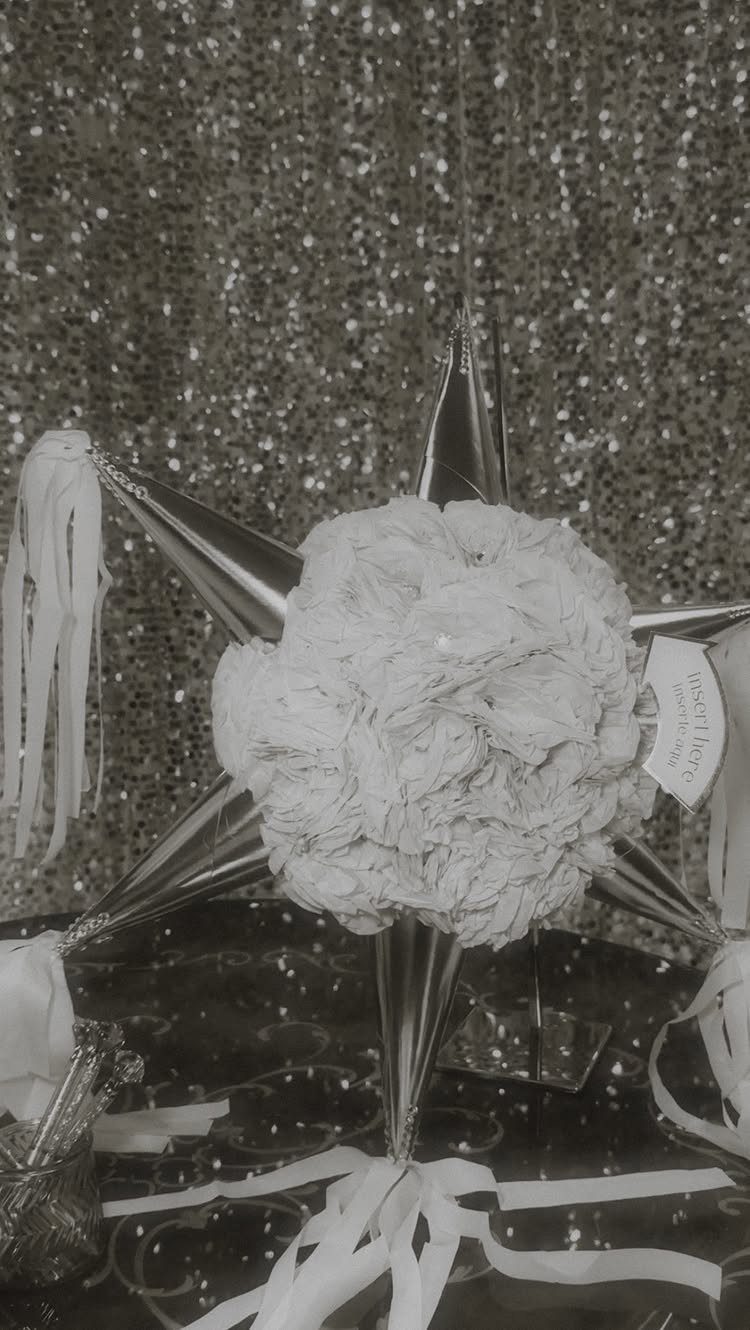 Star-shaped wedding piñata with white floral center against a gold sequin backdrop