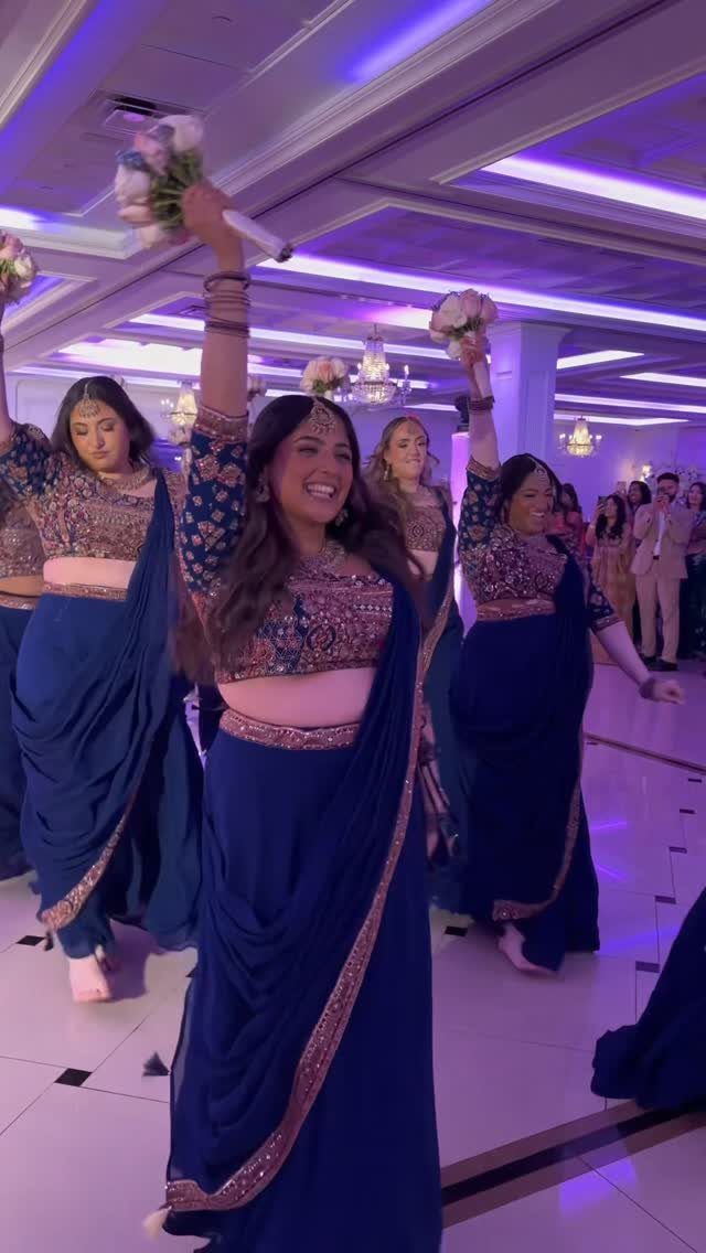 Women in blue sarees dancing and holding flowers at a wedding party.