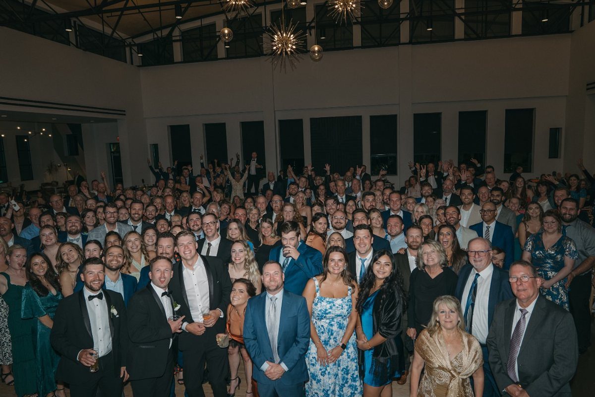 Large group of wedding guests in formal wear posing together in a reception hall.
