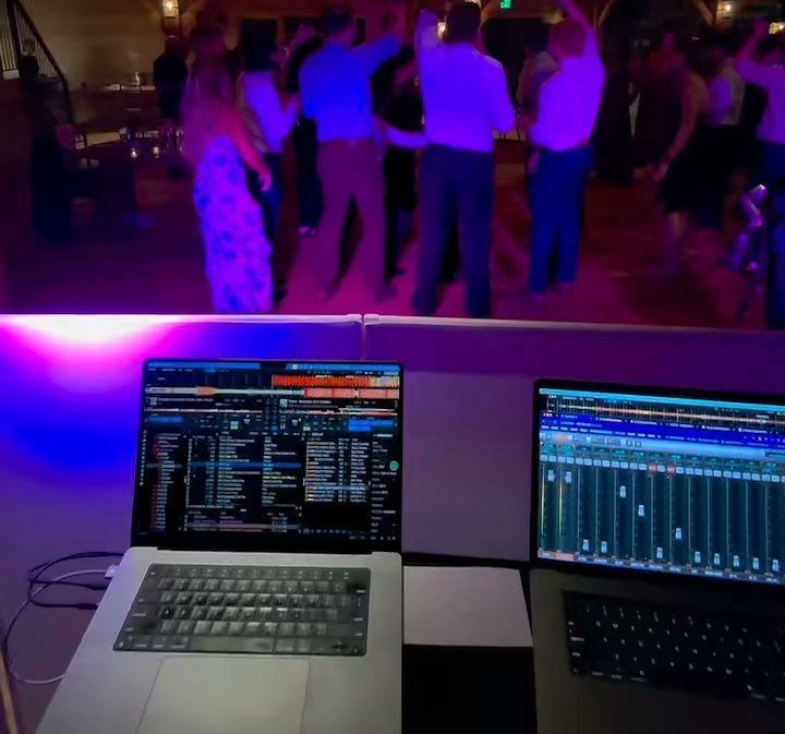 DJ laptops with music software in foreground, wedding guests dancing in blurred background