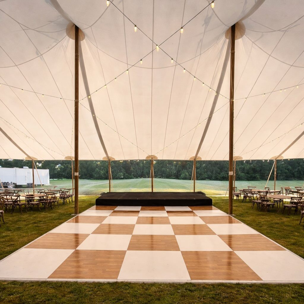 Checkered dance floor under a white event tent with string lights and outdoor seating.