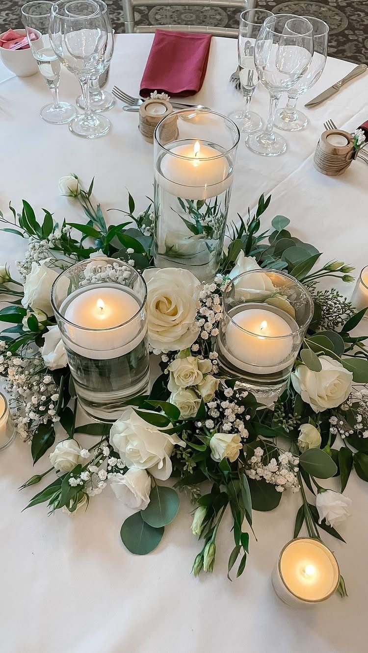 Floating white candles in glass cylinder vases surrounded by white roses and greenery.