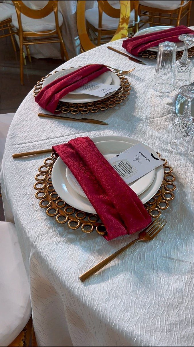 Gold charger plates with white dinner plates and burgundy napkins on a white table.