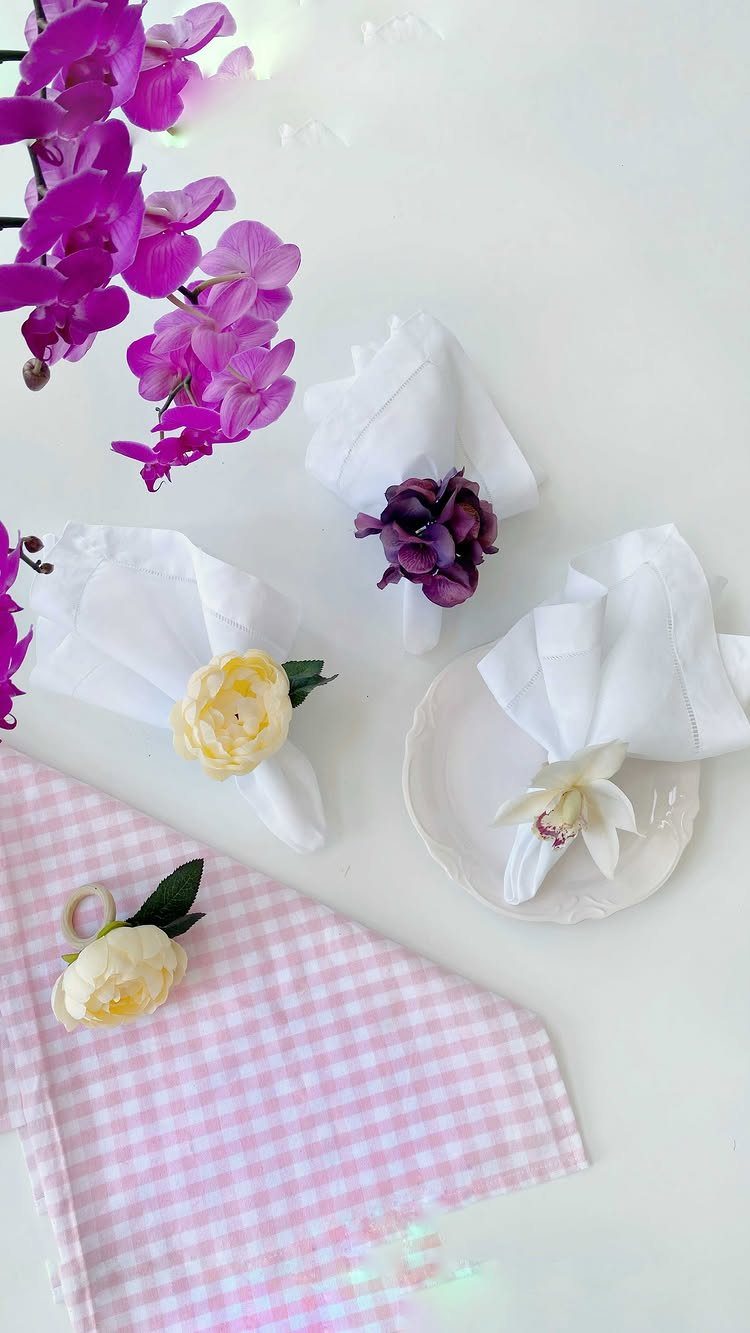 White napkins with artificial flower rings on a white surface with purple orchids.