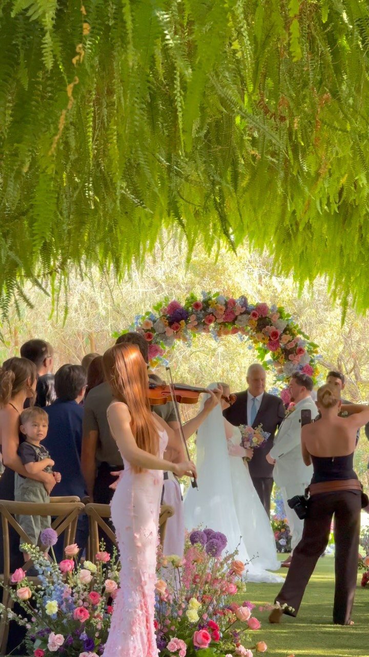Violinist playing for a bride and groom under a colorful floral wedding arch.